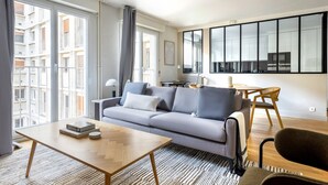 A modern living room with a grey sofa, a wooden coffee table, and a dining area with a small table and chairs. - Blueground | Porte de Champerret, elevator (Paris)