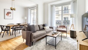 A modern living room with a grey sofa, a coffee table, and a dining area with a wooden table and chairs. - Blueground | Rochechouart, nr Rue de Martyrs (Paris)