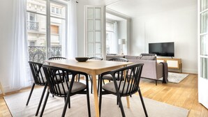 A modern living room with a dining area, large windows, a flat-screen TV, and a balcony. - Blueground | Rochechouart, nr Rue de Martyrs (Paris)