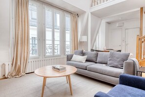 A living room with a grey sofa, a round wooden coffee table, and a blue armchair. - Blueground | Jardin des Plantes, fully furnished (Paris)