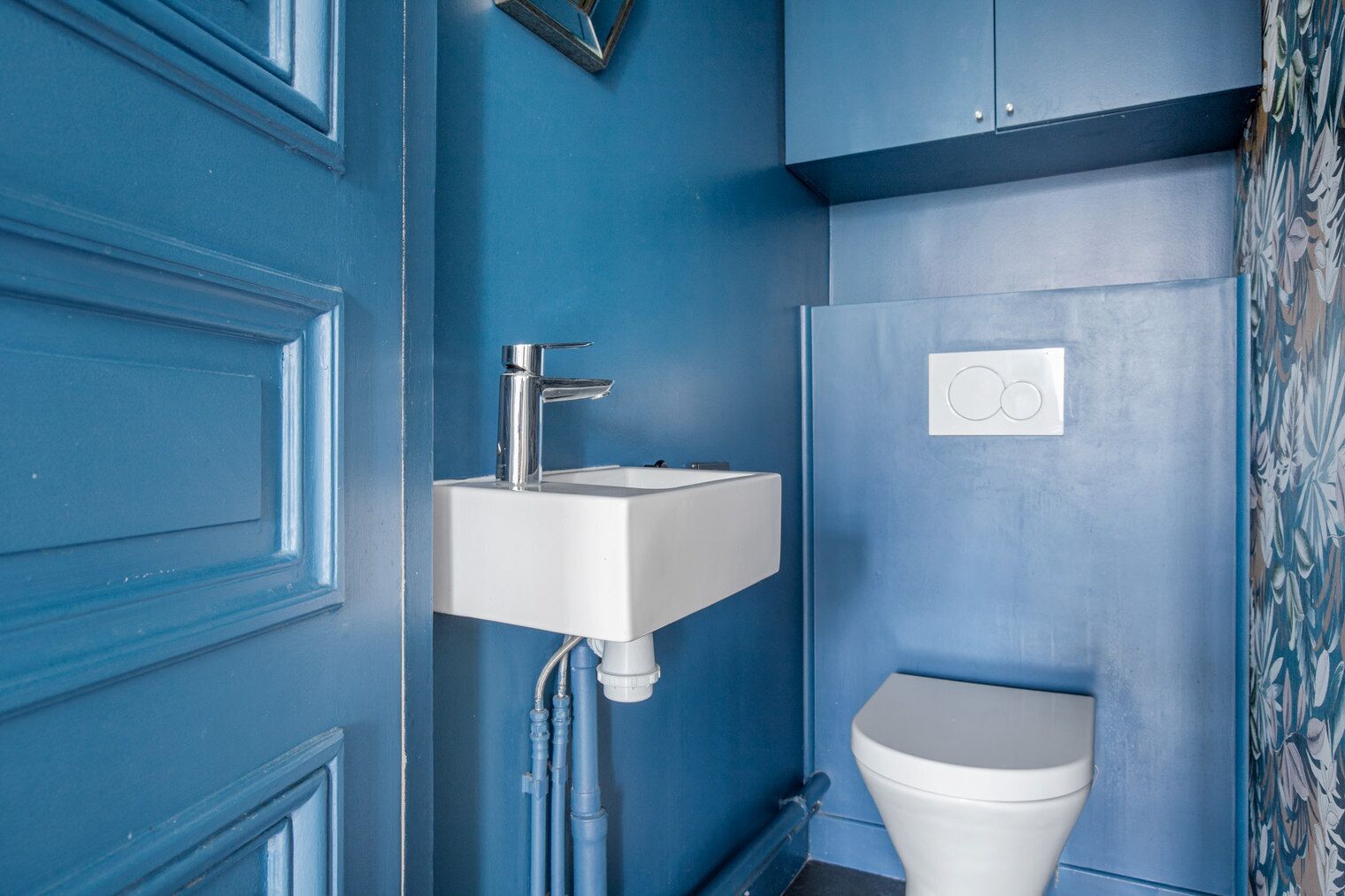 Casa de banho com lavatório branco, sanita e parede azul.