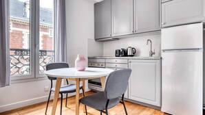 Une cuisine moderne avec des meubles gris, un plan de travail blanc, un réfrigérateur en acier inoxydable et une table ronde accompagnée de deux chaises.