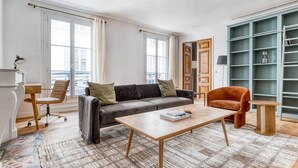 A living room with a grey sofa, a wooden coffee table, a red armchair, a small side table, and a bookshelf.
