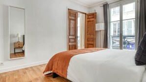 A bedroom with a bed, a nightstand, a mirror, and a window with curtains.