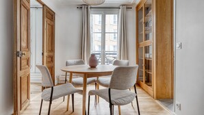 A dining area with a round table, four chairs, a vase, and a hanging light fixture.