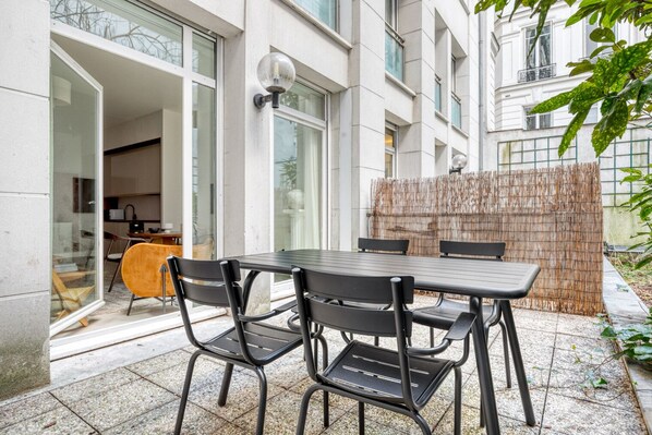 A patio with a table and chairs, a wooden fence, and a building with large windows and a door. - Blueground | Saint Georges, terrace, nr Montmartre (Paris)