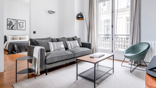 Una sala de estar moderna con un sofá gris, una mesa de centro, una lámpara de pie negra y un sillón turquesa.