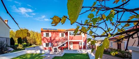 Una casa roja de dos pisos con un césped bien cuidado, una escalera visible y un cielo azul despejado.