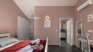 Ein Hotelzimmer mit einem Bett, einer roten Tagesdecke, Handtüchern, einem Blumenstrauß, einem Spiegel und einer Tür zu einem Badezimmer.