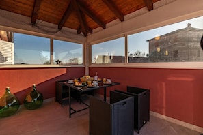 Un comedor con una mesa lista para el desayuno, ventanas amplias y vistas a un edificio.