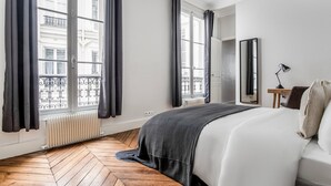 Un dormitorio con una cama grande, una mesita de noche con lámpara, un espejo y vistas al balcón exterior.