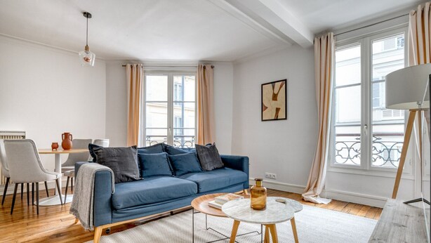 A modern living room with a blue sofa, a round coffee table, and a dining area with a white table and chairs. - Blueground | Villiers/Batignolles, fully furnished (Paris)
