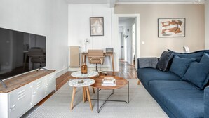 A modern living room with a TV, sofa, coffee table, and a dining area with chairs and a table. - Blueground | Villiers/Batignolles, fully furnished (Paris)