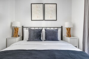 Une chambre d’hôtel moderne avec un grand lit, deux tables de chevet avec des lampes et deux œuvres d’art encadrées accrochées au mur.