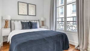A bedroom with a bed, two bedside tables, a window with curtains, and a balcony view. - Blueground | Villiers/Batignolles, fully furnished (Paris)