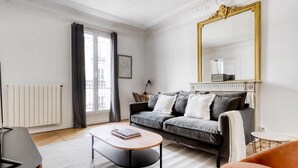 A modern living room with a grey sofa, a round coffee table, and a large mirror with a gold frame. - Blueground | Raspail/Rennes, balcony, furnished (Paris)