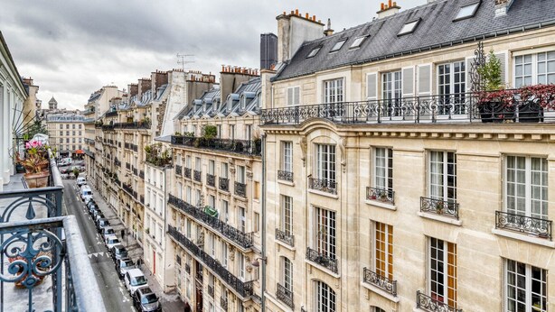 A row of historic European-style buildings with balconies, narrow streets, and parked cars. - Blueground | Raspail/Rennes, balcony, furnished (Paris)