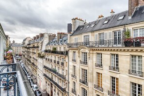 A row of historic European-style buildings with balconies, narrow streets, and parked cars. - Blueground | Raspail/Rennes, balcony, furnished (Paris)