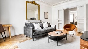 A modern living room with a grey sofa, a wooden coffee table, and a large mirror with a gold frame. - Blueground | Raspail/Rennes, balcony, furnished (Paris)