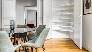 A dining area with a round table, four chairs, and a glass vase. - Blueground | Raspail/Rennes, balcony, furnished (Paris)