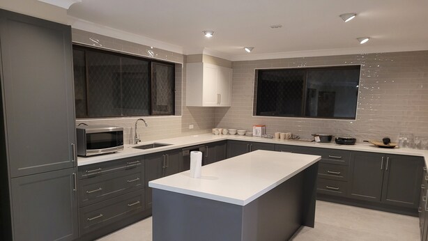A modern kitchen with dark cabinets, a central island, a microwave, and a sink.