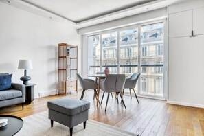 Relax in this stylish living room with a sofa set, round table, and ottoman, offering a view of a nearby building with classical architecture.