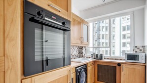 A modern kitchen with wooden cabinets, a built-in oven, a washing machine, and a microwave.