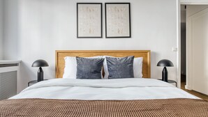 A neatly made bed with a wooden headboard, two bedside lamps, and a patterned rug.