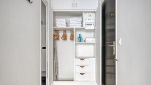 Ein begehbarer Kleiderschrank mit weißen Schränken, einer Kleiderstange und einem Ablagebereich für gefaltete Handtücher.