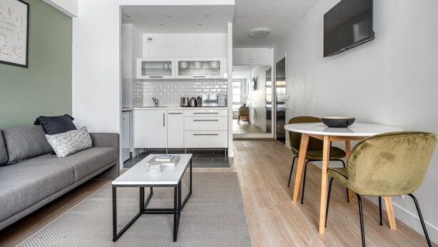 Ein modernes Wohnzimmer mit grauem Sofa, einem Couchtisch und einem Essbereich mit Tisch und Stühlen.