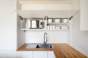 A compact kitchen with a built-in microwave, a stainless steel sink, and white cabinetry.