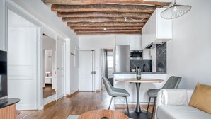 A modern living room with a wooden ceiling, a dining area with a round table, and a kitchen in the background. - Blueground | Sèvres, near shopping (Paris)
