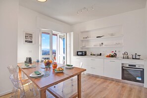 Une cuisine moderne avec des meubles blancs, une table à manger en bois et une vue sur l’extérieur grâce à une grande fenêtre.