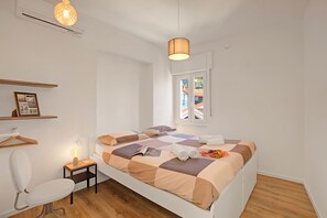 Een slaapkamer met een bed, een stoel, een nachtkastje met een lamp, een hanglamp en een raam met uitzicht.