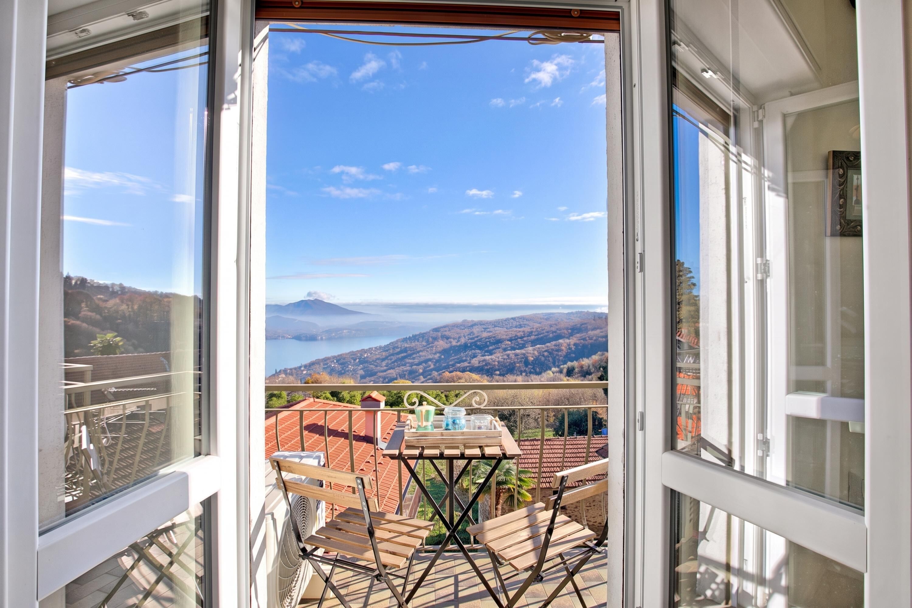 A balcony with a table and chairs, overlooking a scenic landscape with hills and a body of water.
