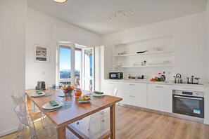 Een moderne keuken met witte kasten, een eettafel met transparante stoelen en uitzicht door de open deur.