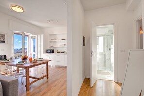 A modern kitchen with white cabinets, a wooden dining table, and a view of the outdoors through the windows.