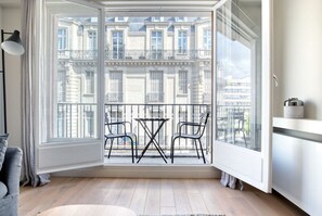Ein Zimmer mit Balkon und Blick auf eine Reihe klassischer europäischer Gebäude. Auf dem Balkon befinden sich zwei Stühle und ein kleiner Tisch.