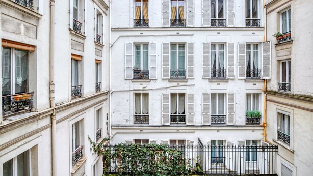 Un immeuble à plusieurs étages, doté de façades blanches, de volets et de balcons.