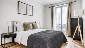 Une chambre à coucher avec un lit, des tables de chevet, une lampe sur pied et une fenêtre avec des rideaux.