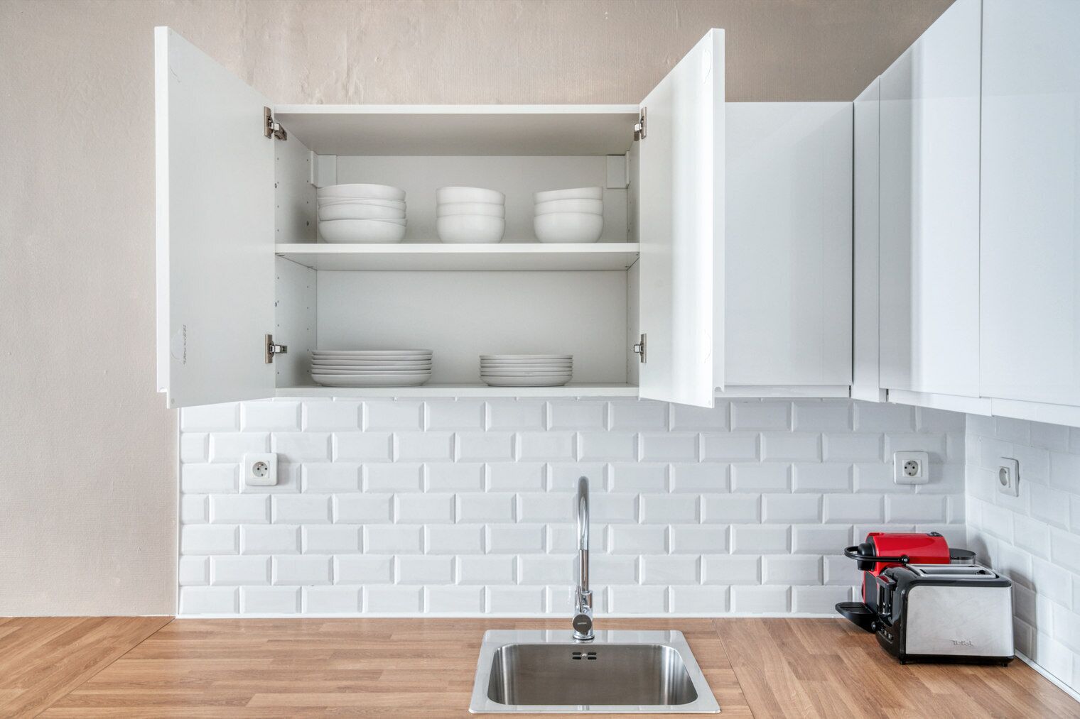 Una cocina con armarios blancos, salpicadero de ladrillo blanco, pileta de acero inoxidable y un tostador rojo.