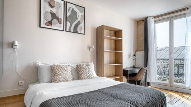 A modern bedroom with a large bed, a wooden desk, and a balcony with a view. - Blueground | Montorgueil/Sentier, nr dining (Paris)