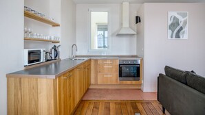 A compact kitchen with wooden cabinets, a built-in microwave, a sink, and an oven. There is a window above the sink and a framed abstract painting on the wall. - Blueground | Montorgueil/Sentier, nr dining (Paris)