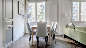 A modern living room with a dining area, large windows, and a view of buildings. - Blueground | Arc de Triomphe, nr shopping (Paris)