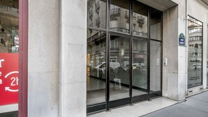 A building facade with large glass windows, a visible street sign, and a red sign with white text on the left. - Blueground | Arc de Triomphe, nr shopping (Paris)