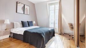 Une chambre moderne avec un lit, des lampes de chevet, une fenêtre avec des rideaux et un fauteuil.