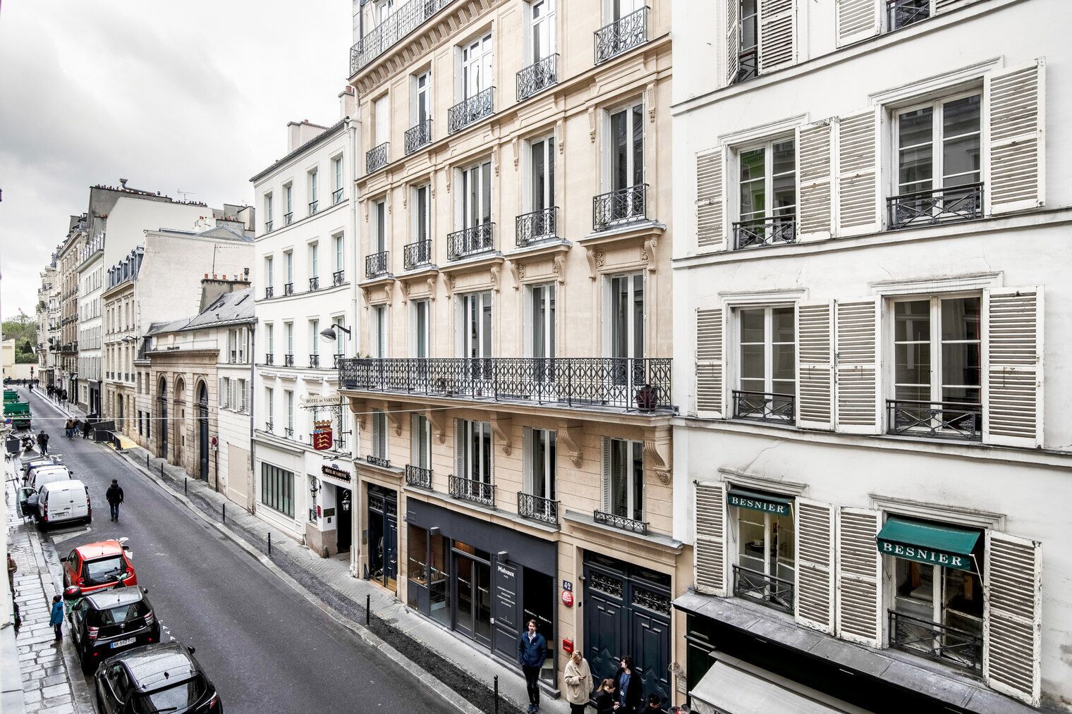 Une vue de rue d’une rangée d’immeubles à plusieurs étages, avec des boutiques au rez-de-chaussée, dont une enseigne d’hôtel bien visible.