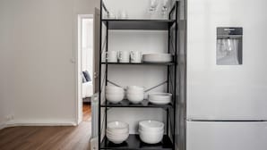 A kitchen with a black metal shelf unit holding white dishes, bowls, and glasses.
