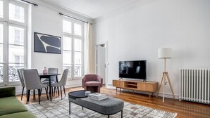 A modern living room with a sofa, a dining table with chairs, a TV on a wooden stand, and a floor lamp.