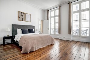 A spacious bedroom with a large bed, wooden flooring, and large windows offering a view of the city. - Blueground | Invalides, nr Rodin Museum (Paris)